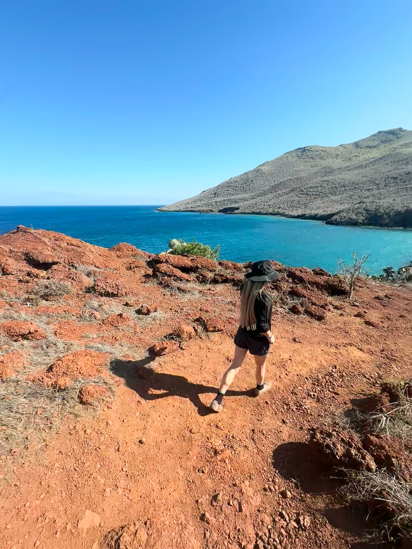 Nicci Grotefendt hiking a red-earth trail above turquoise Galápagos waters
